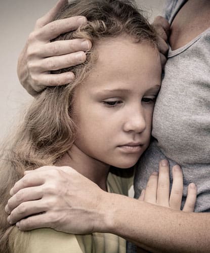 A young girl looking sad while getting a hug.