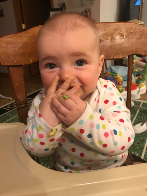 infant eating avocado in a high chair