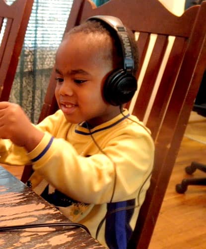 Preschool African American boy wearing headphones playing with play dough while listening to therapeutic music. 