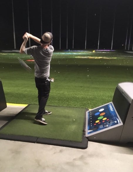 golfing man swinging a golf club at a top golf range