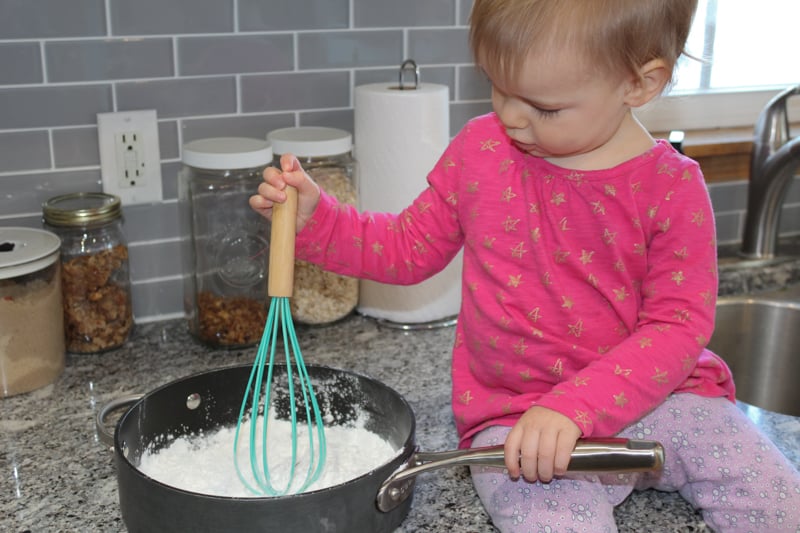 young girl sitting on counter stirring the dry ingredients for gluten free playdoh in a saucepan which stimulates the vestibular system.
