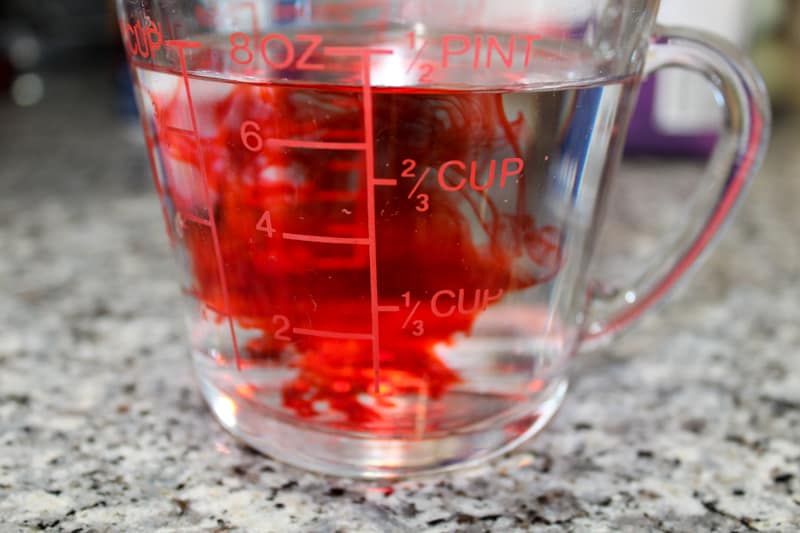 red food coloring spreading out in a measuring cup of water sitting on the counter