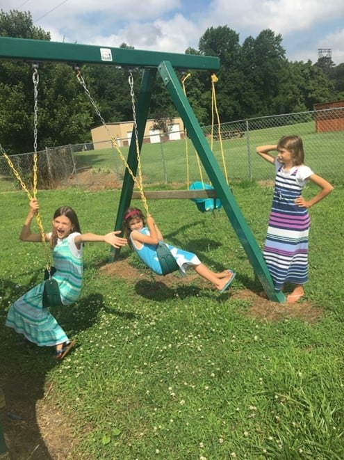 spinning-on-swingset Two girls twisting the swings on a swing set and one girl standing to the side