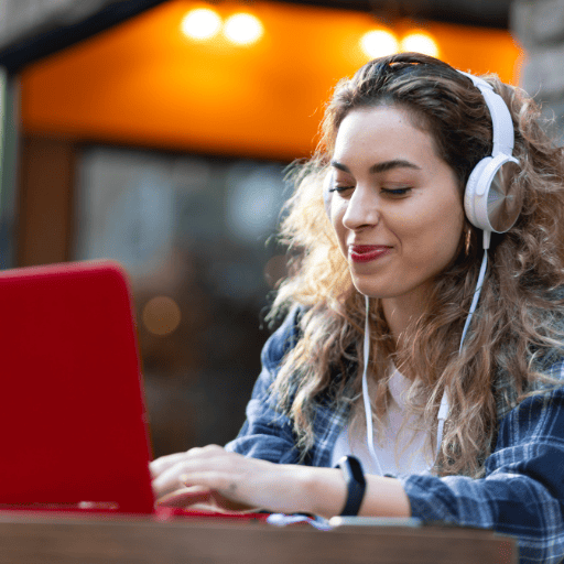 young lady wearing headphones working on a red laptop outside a cafe