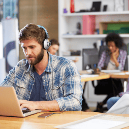 college aged man working on a laptop while wearing headphones in a library