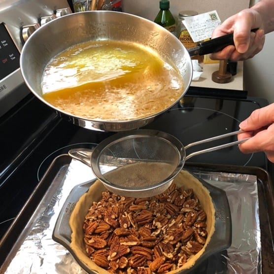 pouring glaze mixture over the pecans in the pie crust