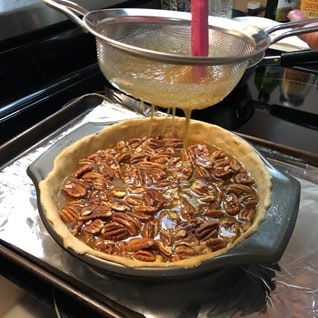 stirring mixture in a fine mesh strainer over a pecan pie
