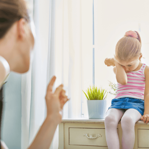 Little girl sitting on a dresser crying while the mother is pointing a finger at her for a behavior related to unknown hearing loss.