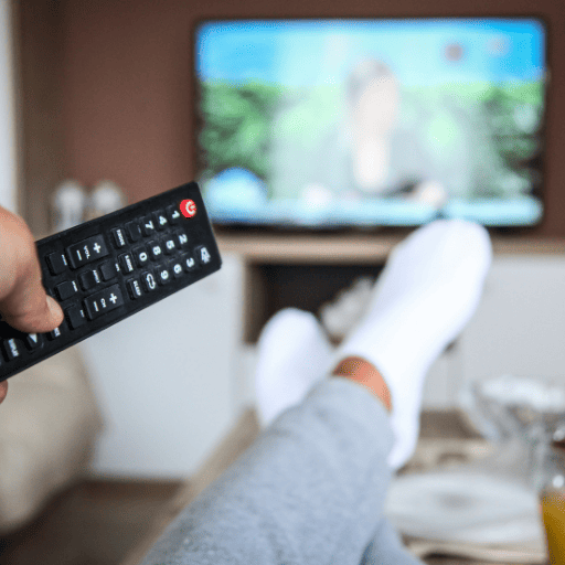holding a tv remote pointed at the TV with feet up on the coffee table