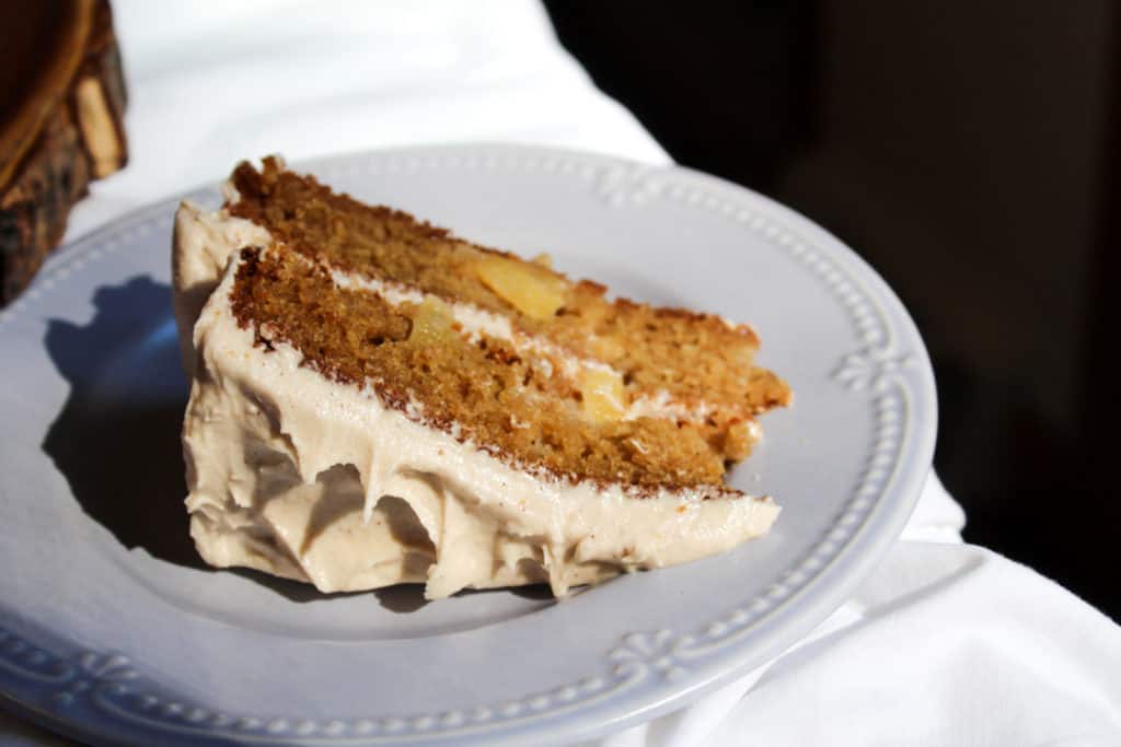 One slice of cake on a small light blue plate sitting in the sunlight. The plate is sitting on white linen. The linen stops at the edge of the plate and the background is black in a triangular shape in the upper right corner.
