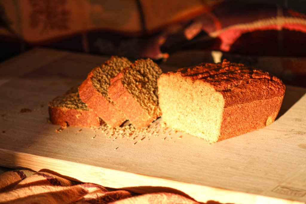 three slices of gluten free pumpkin bread leaning over on a wooden cutting board. The rest of the loaf is rotated 20 degrees towards the camera. The image is warm with a strong amber tone. 