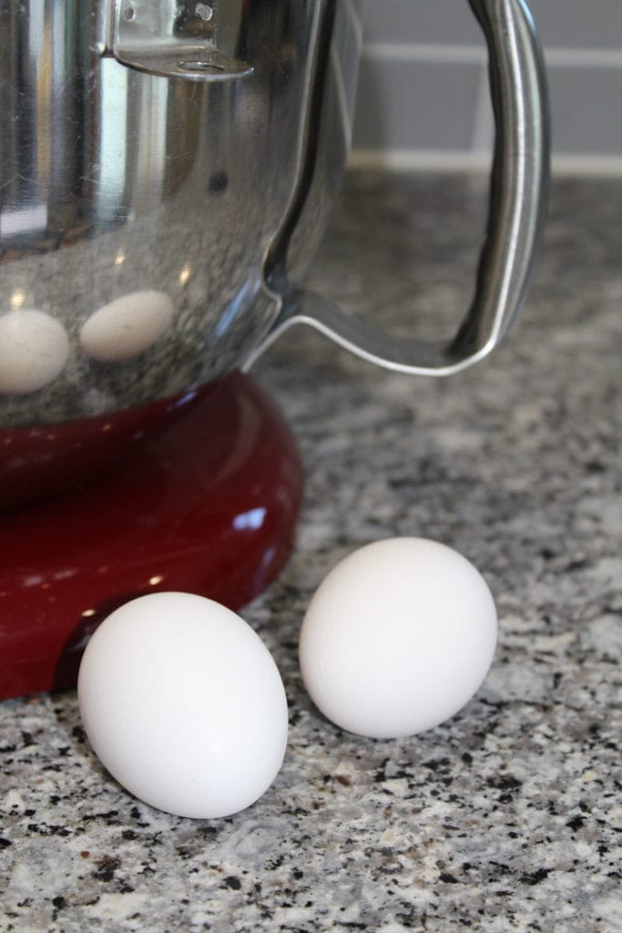 two white eggs sitting on the counter in front of a kitchen aid mixer with a red stand. 