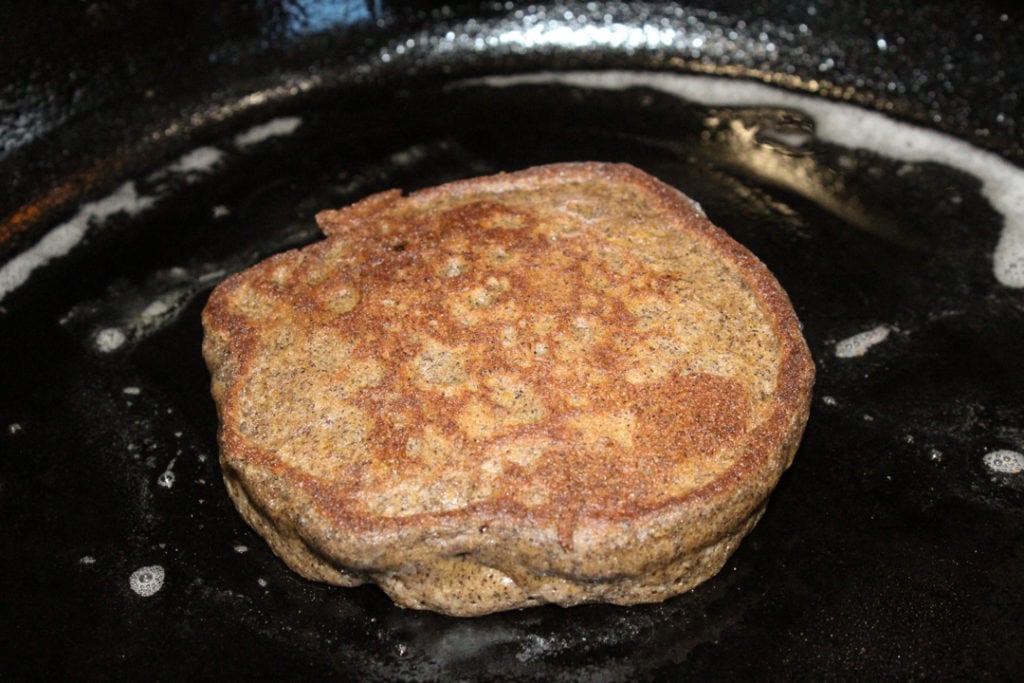 Gluten and dairy free pumpkin spice pancake cooking in a cast iron skillet. 