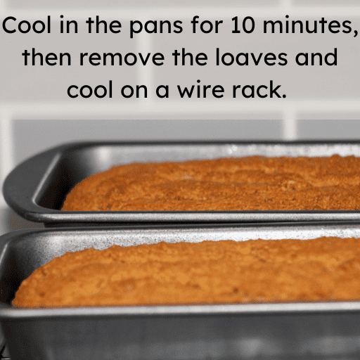 two gluten free pumpkin bread loaves cooling in their pans on a cooling rack. The background is a gray subway tile backsplash.