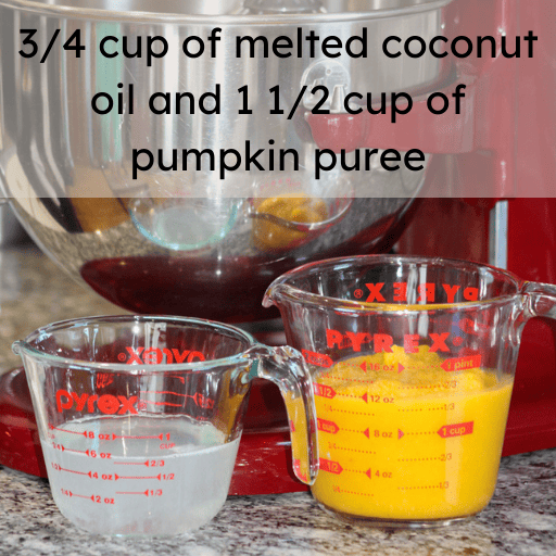a one cup glass measuring cup with melted coconut oil sitting on the counter next to a two cup glass measuring cup with pumpkin puree. They are sitting in front of a red kitchenaid mixer with the stainless steal mixing bowl attached.  Ingredients and measurements are listed at the top of the image. 