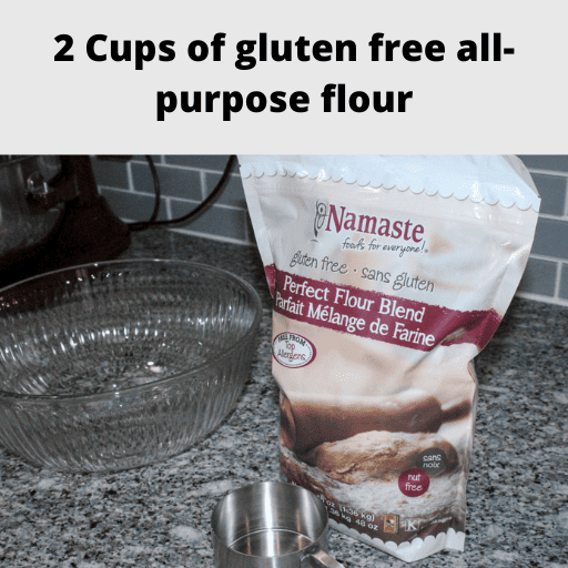 On the left there is a large empty glass bowl. On the right is a bag of Namaste gluten free flour with a stainless steal 1 cup measuring cup sitting in front of it. 