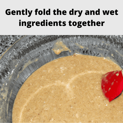 All the ingredients for a gluten and dairy free apple spice cake mixed together in a large glass bowl minus the apple chunks. There is a red spatula leaning on the right side of the bowl with a wooden handle.