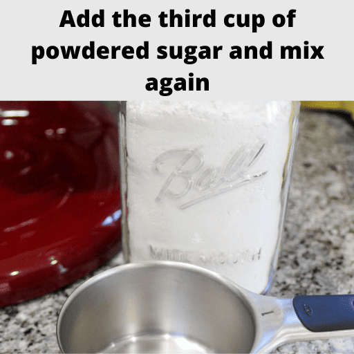 A one cup measuring cup sitting on the counter in front of a mason jar of powdered sugar. Behind them on the left is a red mixer stand. On the right are cooling racks with a yellow tea towel draped overtop.