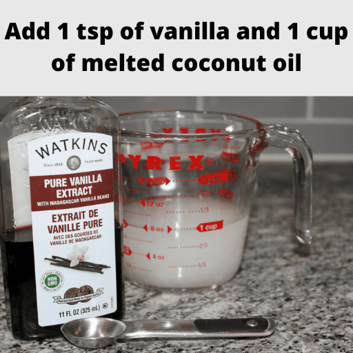 In the foreground there is a stainless steal 1 tsp measuring spoon next to a container of vanilla. Behind them is a glass liquid measuring cup with 1 cup of melted coconut oil. 