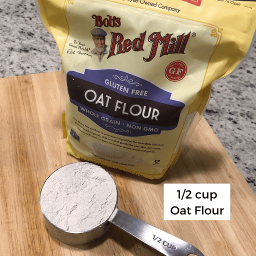 1/2 cup of oat flour sitting on a cutting board in front of a bag of oat flour. 