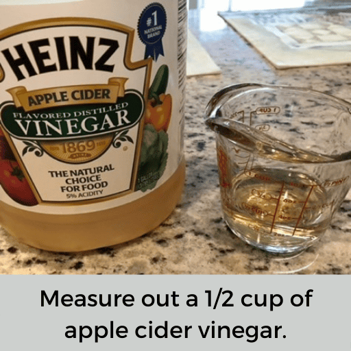 glass measuring cup with a 1/2 cup of apple cider vinegar sitting next to the apple cider vinegar bottle on the countertop. 