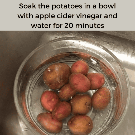 Red potatoes in a glass bowl soaking in an apple cider vinegar and water mixture. The bowl is sitting in a stainless steel sink. There is a gray box with black text at the top. 