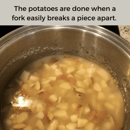 Cooked potatoes for creamy mashed potatoes in a stainless steel pot before they have been strained. There is a gray box with black text at the top.
