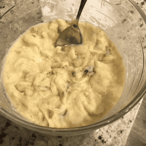 gluten and dairy free creamy mashed potatoes in a glass bowl on the countertop with a serving spoon in it.