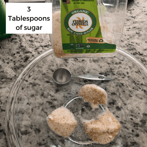 three tablespoons of sugar in three piles in a glass bowl. The bowl is sitting on the countertop and the sugar container is behind the bowl