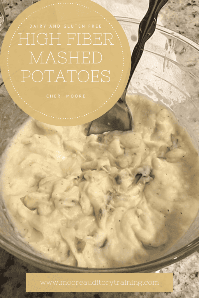 creamy high fiber dairy free mashed potatoes in a glass bowl with a spoon sticking out. The glass bowl is sitting on a grey speckled countertop. In the top left hand corner is a tan circle with white text. In the center at the bottom is another tan box with white text.
