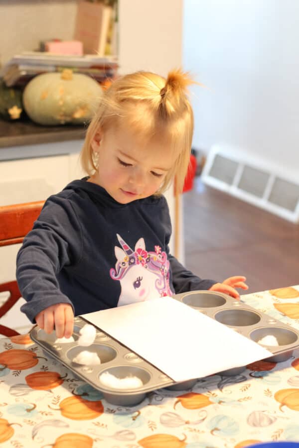 Toddler aged girl sitting at the kitchen table playing the herding sheep game from the Encouraging Observation Through Purposeful Play: Toddler Visual Play booklet