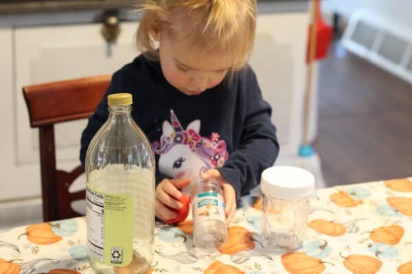Toddler aged girl putting lids on different containers at the kitchen table.