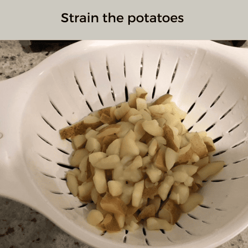chopped potatoes in a white plastic strainer sitting on the countertop for creamy mashed potatoes. There is a gray box with black text at the top. 