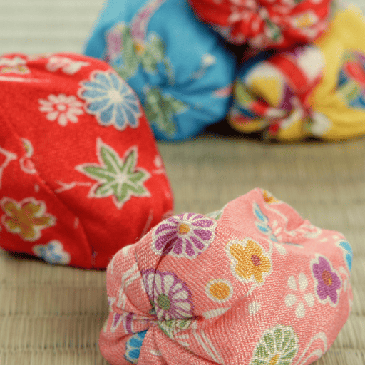 5 colorful bean bags sitting on the ground for a visual-motor activity. In the background, three are stacked like a pyramid. In the foreground two are staggered one in front of the other. The fabric is floral with a solid background. There are two red, one blue, one yellow and one pink bean bag.