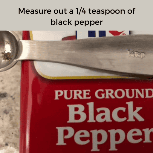 a 1/4 tsp metal measuring spoon sitting on top of a metal tin of black pepper on the countertop. There is a gray box with black text at the top.