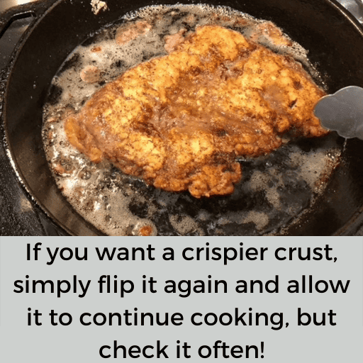 gluten free country fried steak being fried in a cast iron skillet. Metal tongs are on the right side of the steak because it was just flipped over.
