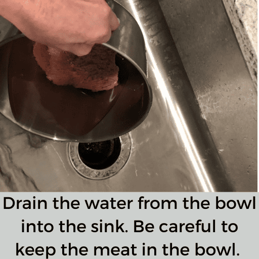 Liquid is being drained out of the bowl into the sink. The meat is still in the bowl. 