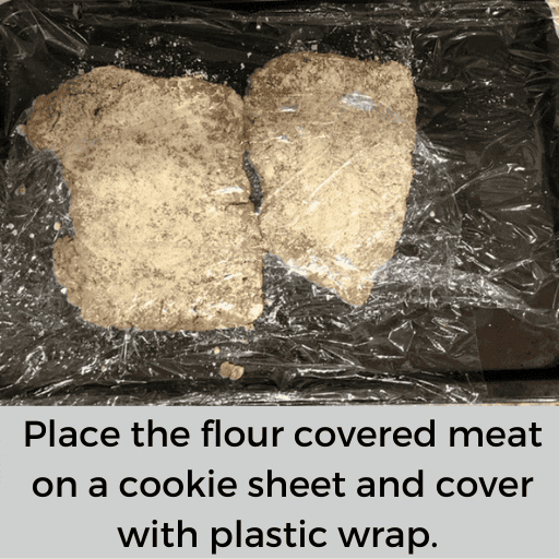two breaded beef cubed steaks sitting on a cookie sheet with plastic wrap overtop