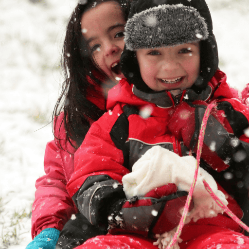 a little boy and girl on a sled in the snow. Both are smiling. 