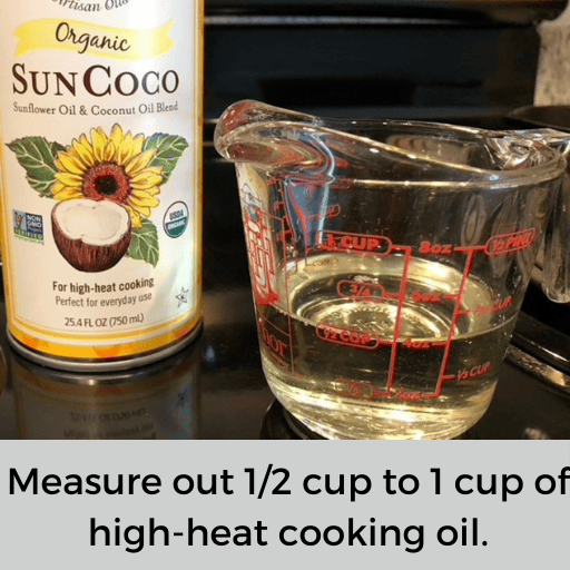 Half cup of sunCoco oil in a glass measuring cup sitting on a black glass stovetop. The bottle of oil is sitting behind the measuring cup. 