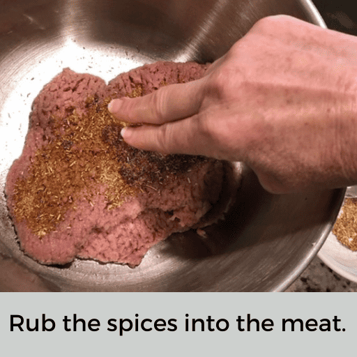 Hand is using two fingers to rub the spices into the beef cubed steak. 