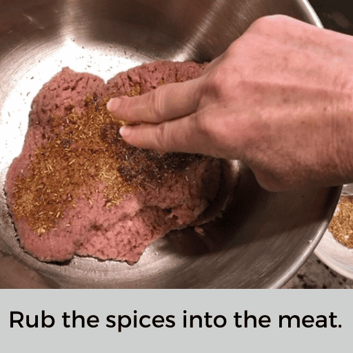 Hand is using two fingers to rub the spices into the beef cubed steak.