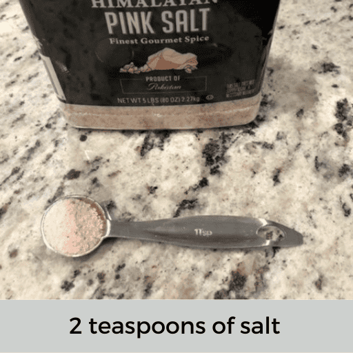 metal teaspoon of salt sitting on the countertop in front of the pink salt container.