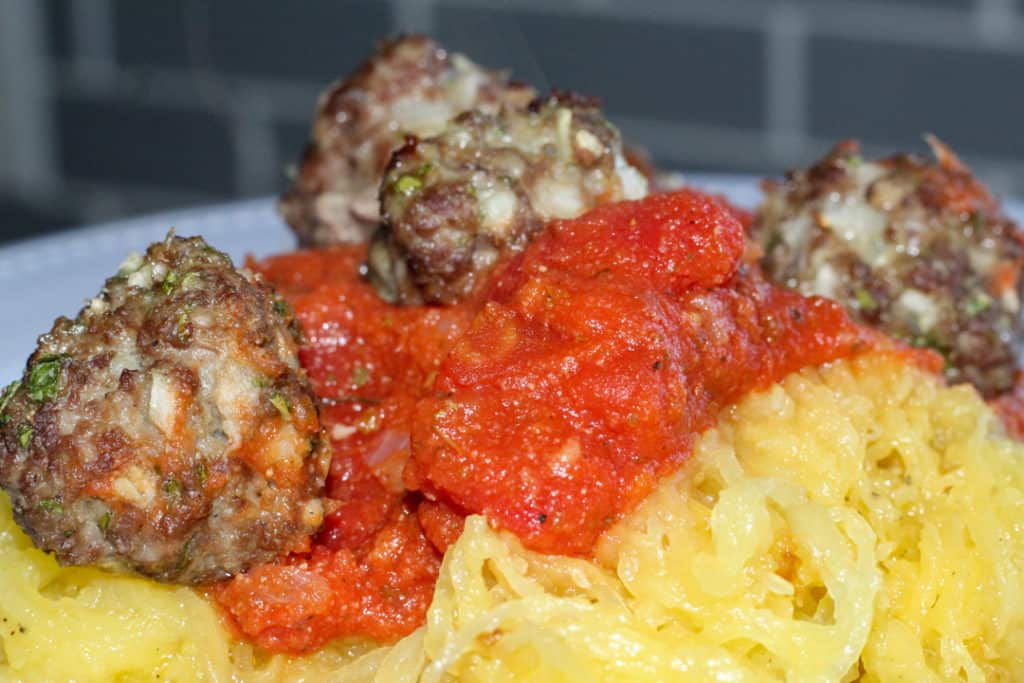 gluten and dairy free meatballs on top of pasta sauce and spaghetti squash