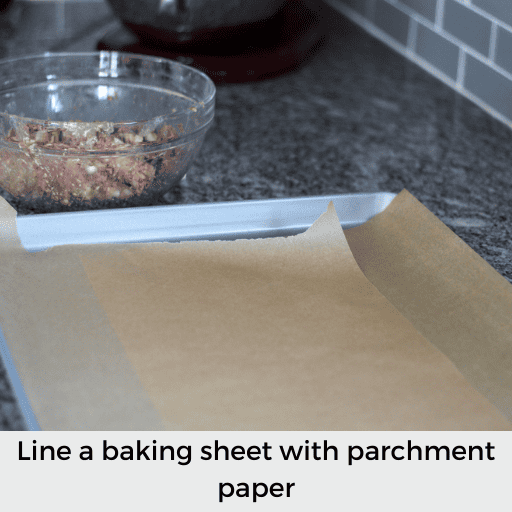large baking sheet lined with parchment paper. It is next to the bowl of gluten and dairy free meatball meat
