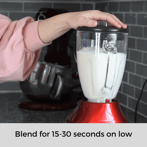 milks in a blender being blended. Person's hand is holding the lid on the blender. 