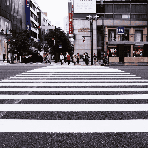 A group of people standing at the far end of a city crosswalk waiting to cross the street. 