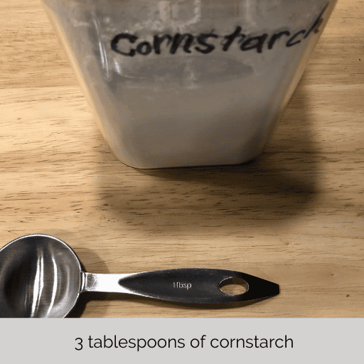 a tablespoon measuring spoon on a cutting board in front of a container of cornstarch