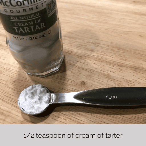 1/2 teaspoon of cream of tarter in a measuring spoon sitting on a cutting board in front of the seasoning bottle