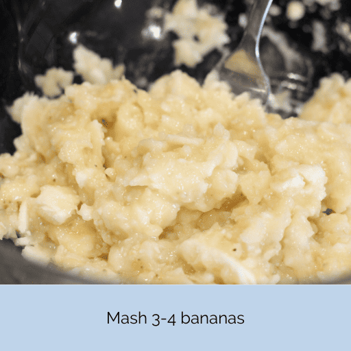 Mashed bananas in a glass bowl with a stainless steel fork. 